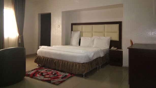 A hotel room with a bed, bedside table, and a desk. - Viclin Diamond Hotels (Abuja)