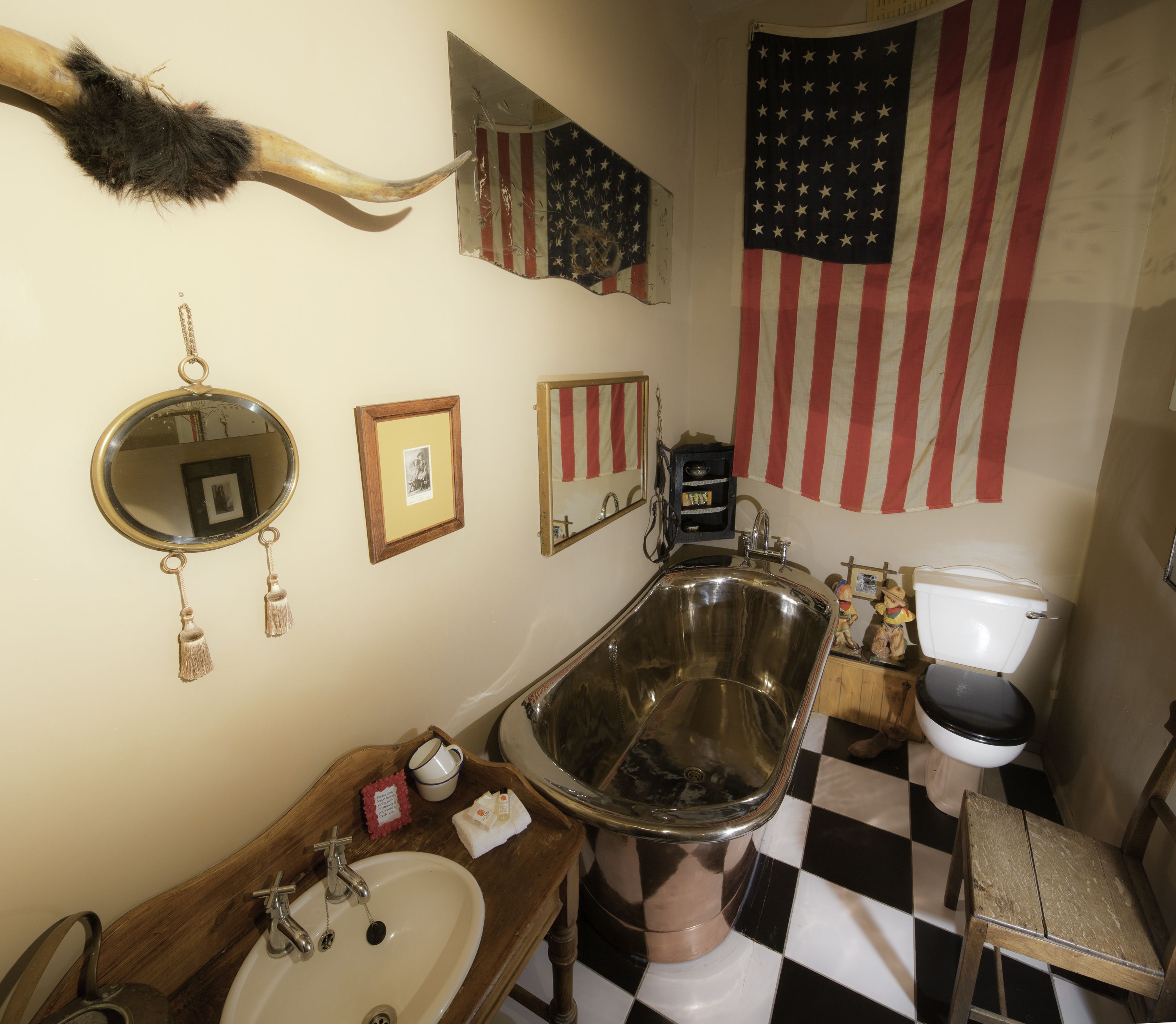A bathroom with a large, ornate bathtub, a sink, a toilet, and various decorations including a large American flag and a mirror with a picture frame.