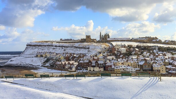 Een kustplaats bedekt met sneeuw, met historische gebouwen, een opvallende kerk en een kasteel op een heuvel.