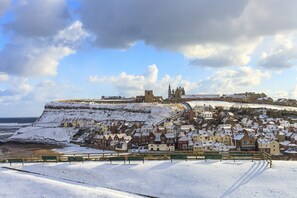 A snow-covered coastal town with historic buildings, a prominent church, and a castle on a hill.