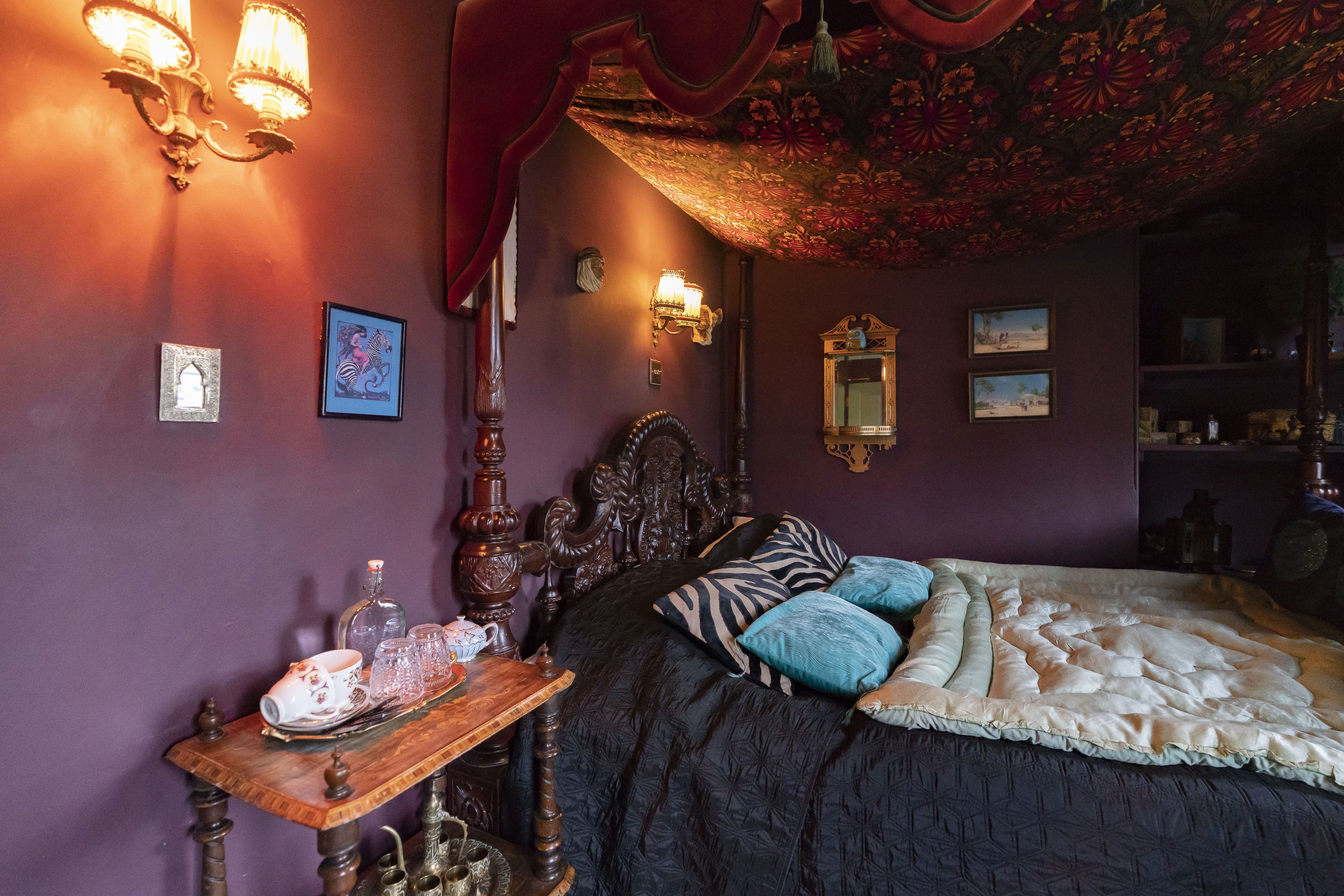 Une chambre à coucher avec un grand lit, une tête de lit décorée et une table de chevet en bois sur laquelle se trouve un plateau avec du matériel pour préparer le thé.