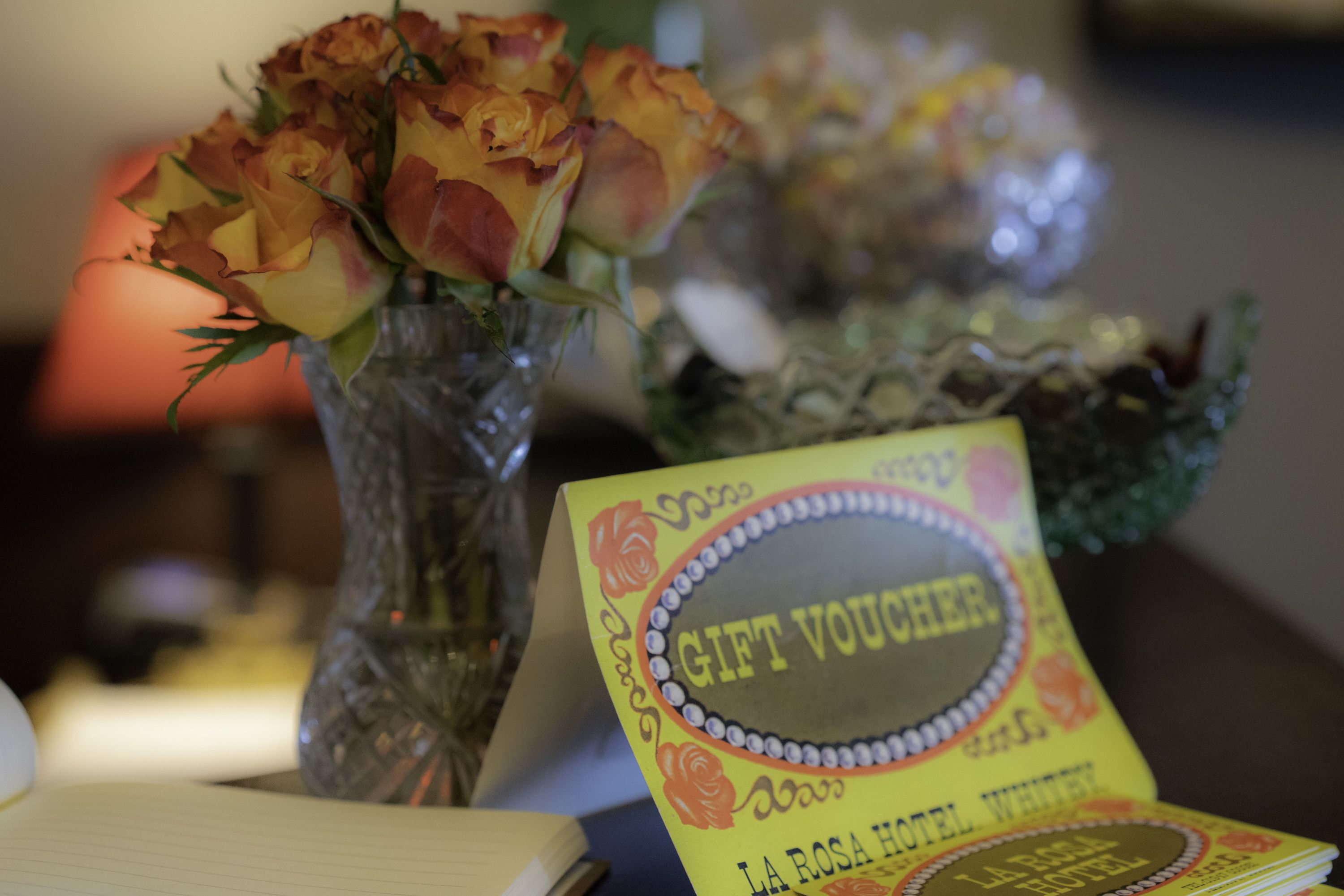 A table with a vase of roses and a gift voucher from La Rosa Hotel.