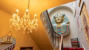 Een statige trap met sierlijk hekwerk, een kroonluchter en een opvallende wanddecoratie met Egyptische motieven.