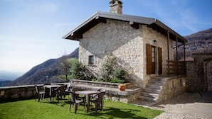 Un edificio de piedra con una escalera de madera, asientos exteriores y vistas a un valle.