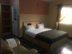 A hotel room with a bed, a chair, a wardrobe, and a window with curtains.