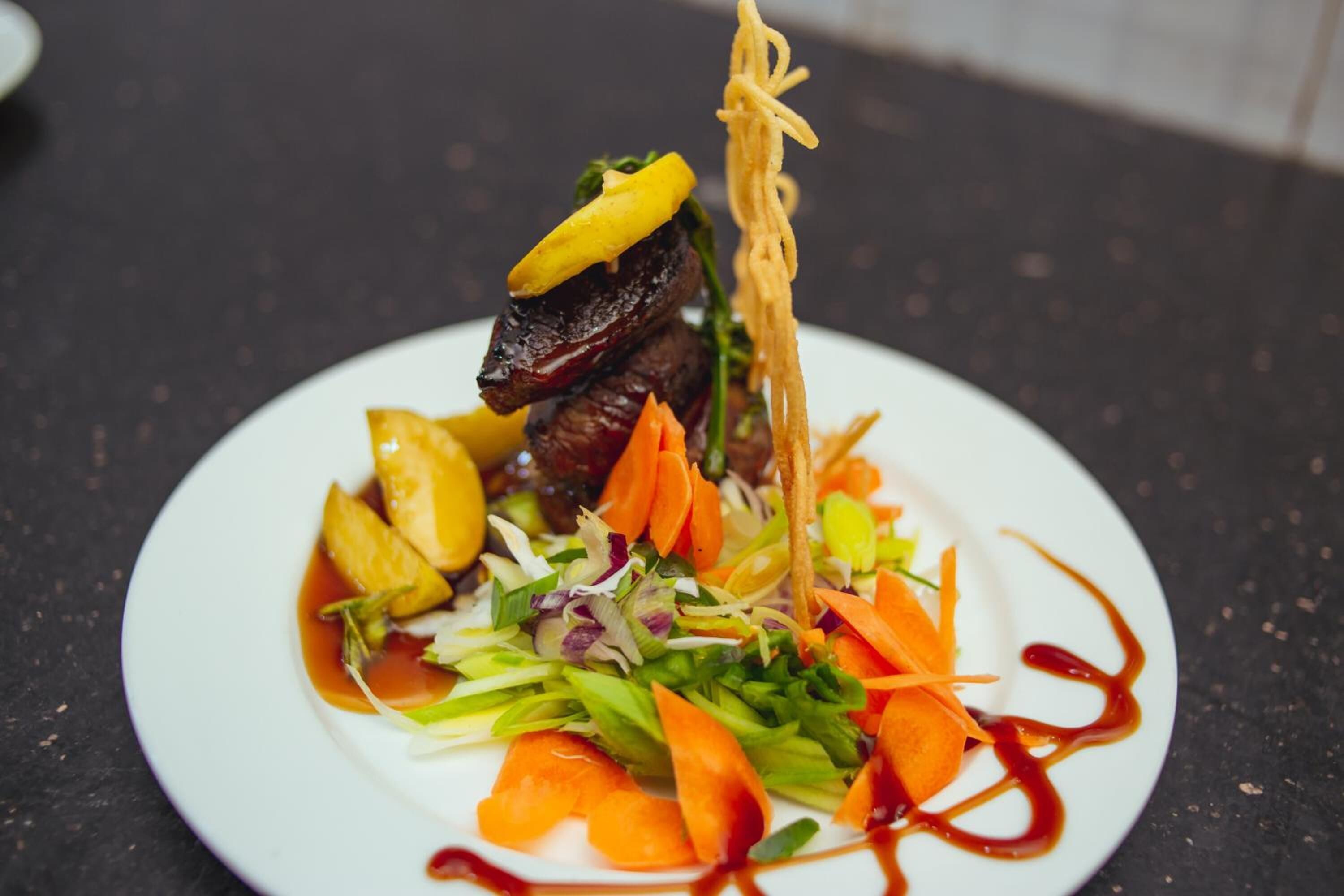 A plate of food with various vegetables and a piece of meat, possibly steak, on a white plate.
