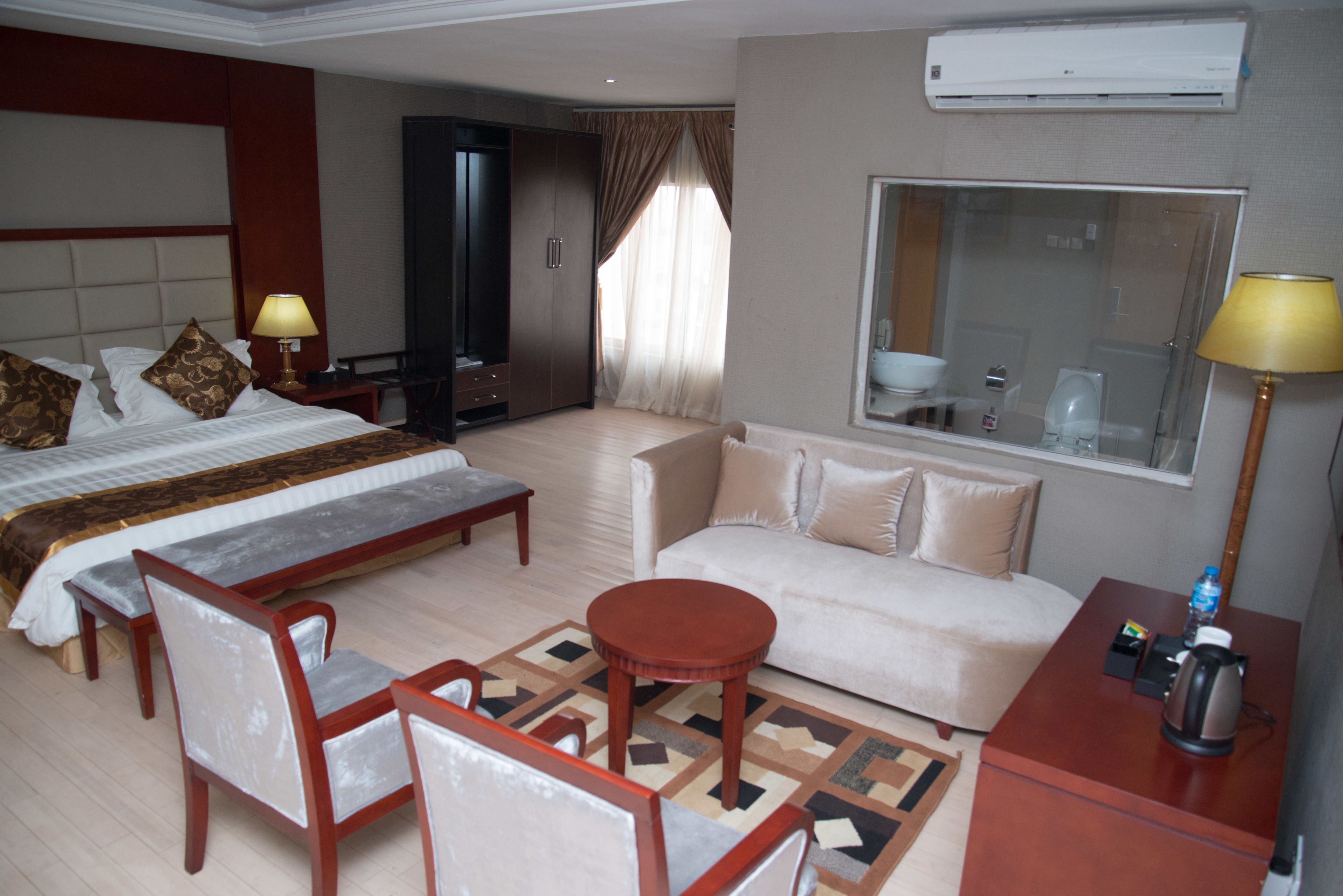 A hotel room with a bed, a sofa, a coffee table, and a desk with a lamp and a kettle.