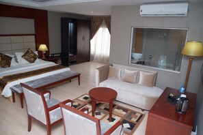 Habitación de hotel con cama, sofá, mesa de centro y escritorio con lámpara y hervidor.