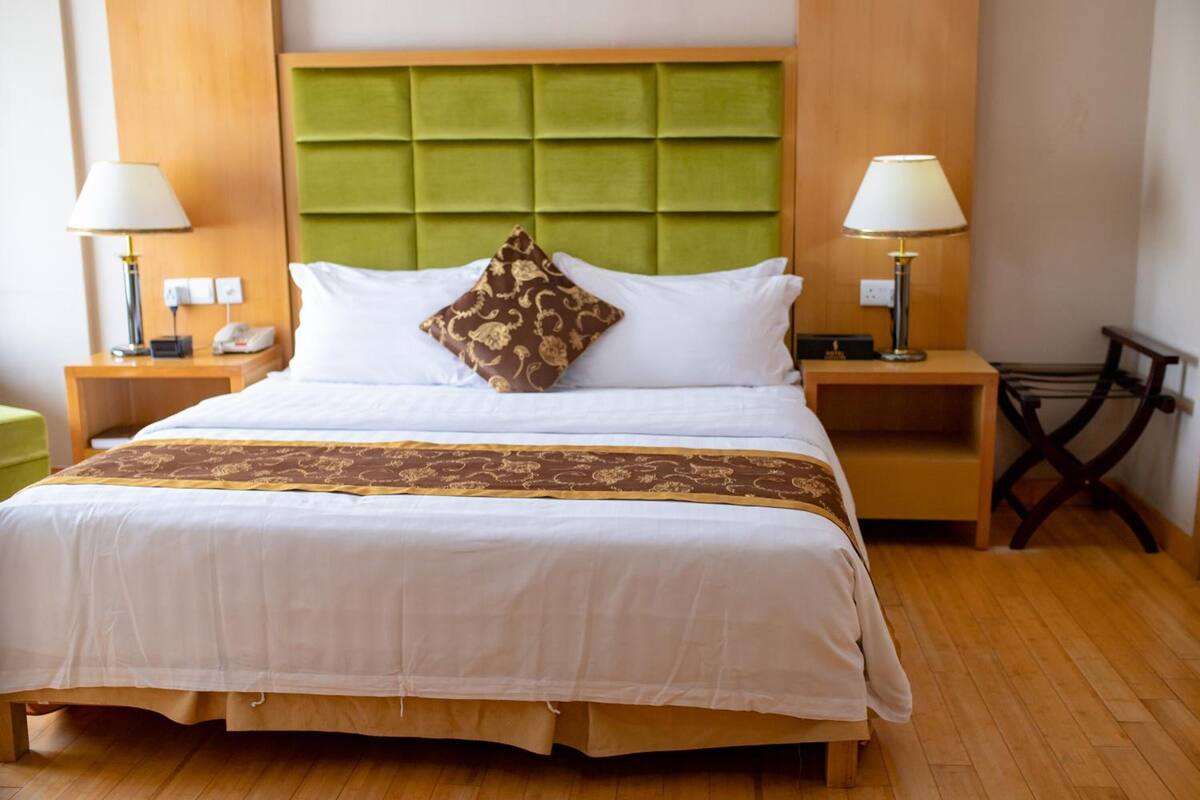 A large bed with a green headboard, white bedding, and a patterned throw blanket. There are two bedside tables with lamps and a bedside phone.