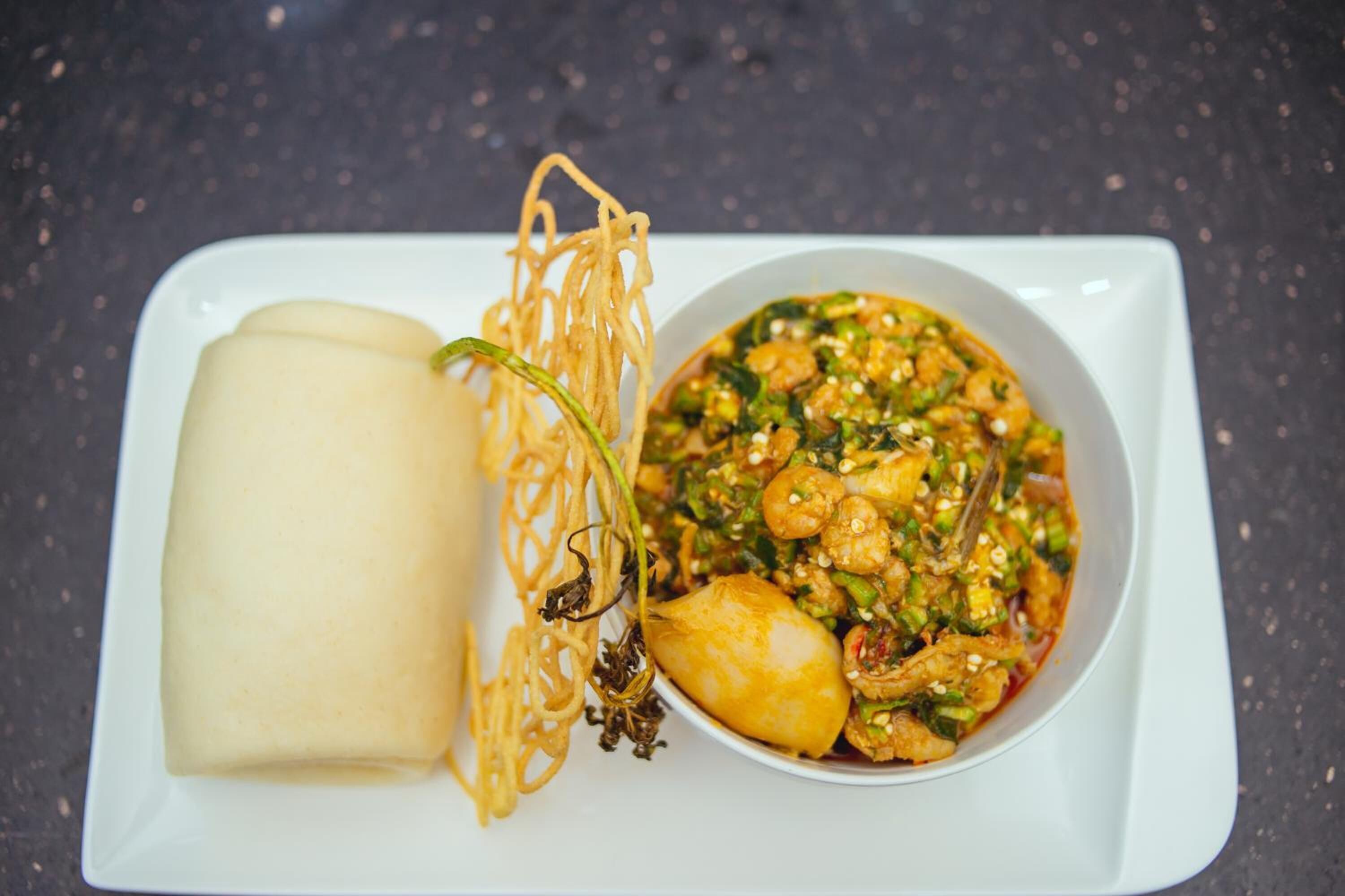 A plate with a white rectangular object, possibly a dessert, and a bowl of food with vegetables and a sauce.
