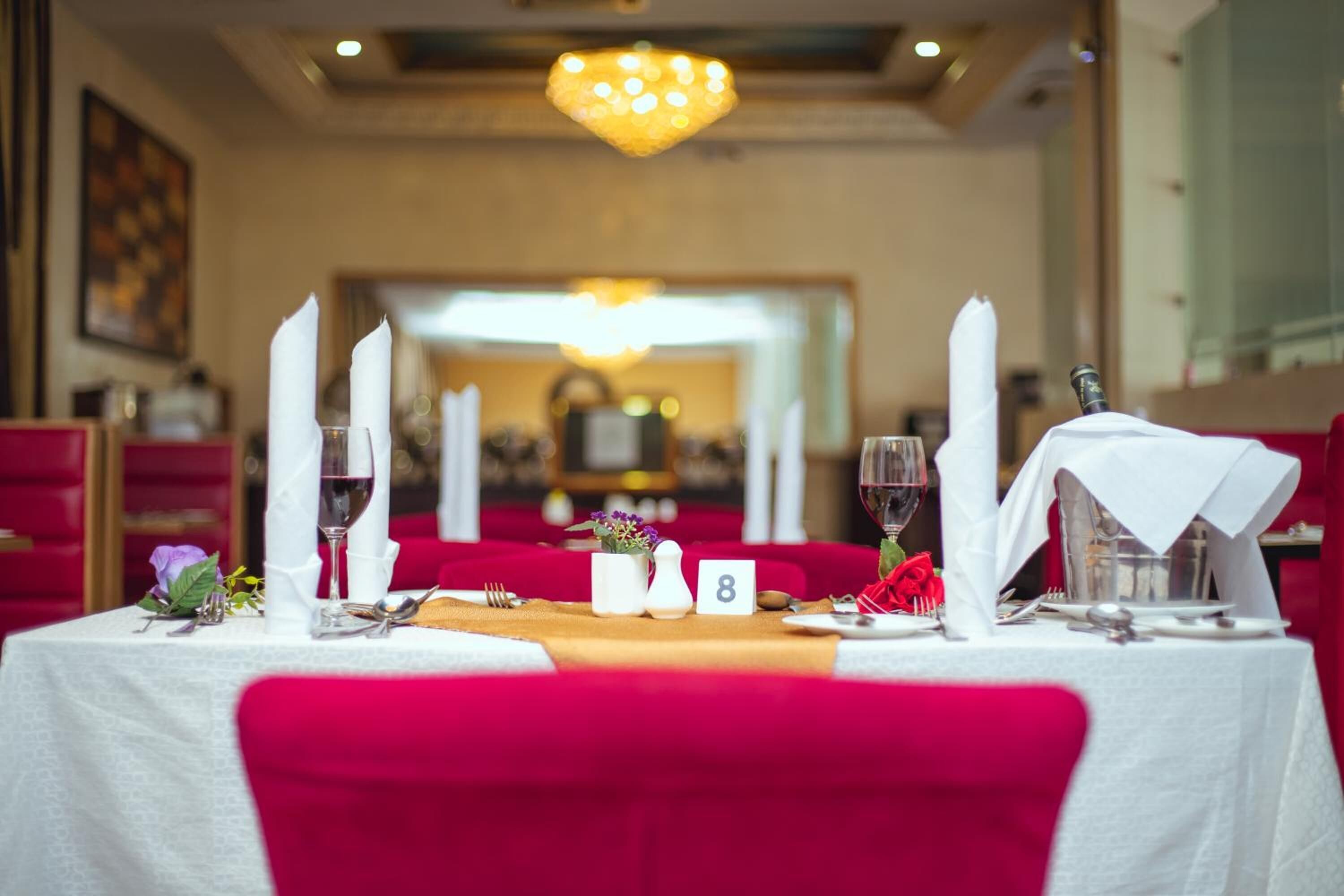 A dining table set with white tablecloth, red chairs, and a chandelier overhead.