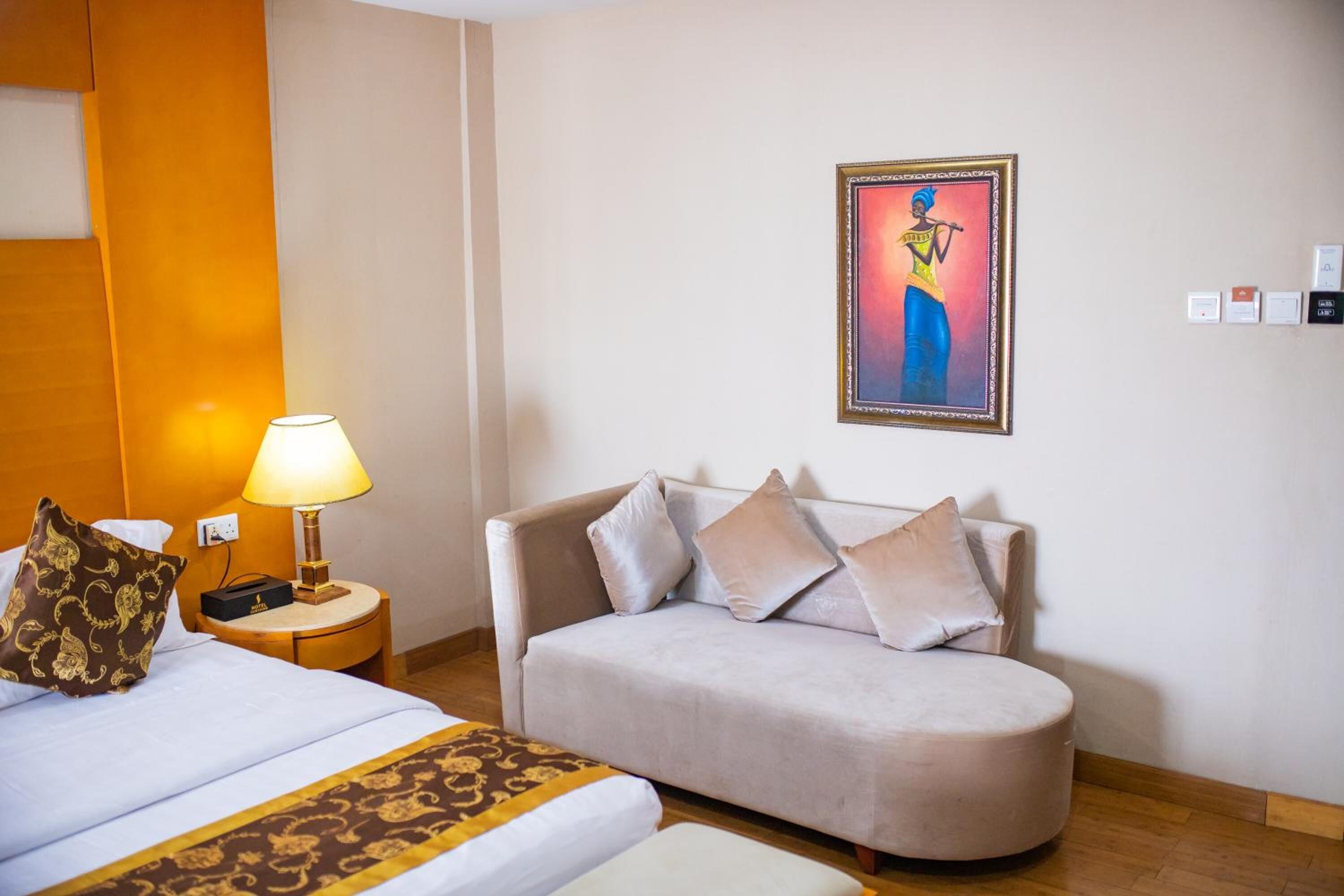 Une chambre d’hôtel avec un lit, un canapé, une lampe, un tableau et une table de chevet.
