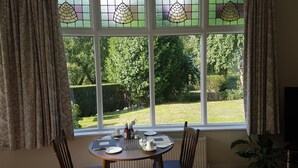 Un coin repas avec une table dressée pour deux personnes, une fenêtre ornée de vitraux et une vue sur un jardin bien entretenu.