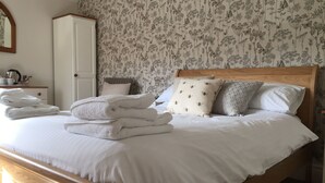 Un lit bien fait, avec du linge de lit blanc et un papier peint à motifs floraux.
