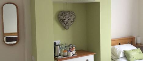 A bedroom with a bed, a dresser, a television mounted on the wall, a heart-shaped decoration, and a trash can.
