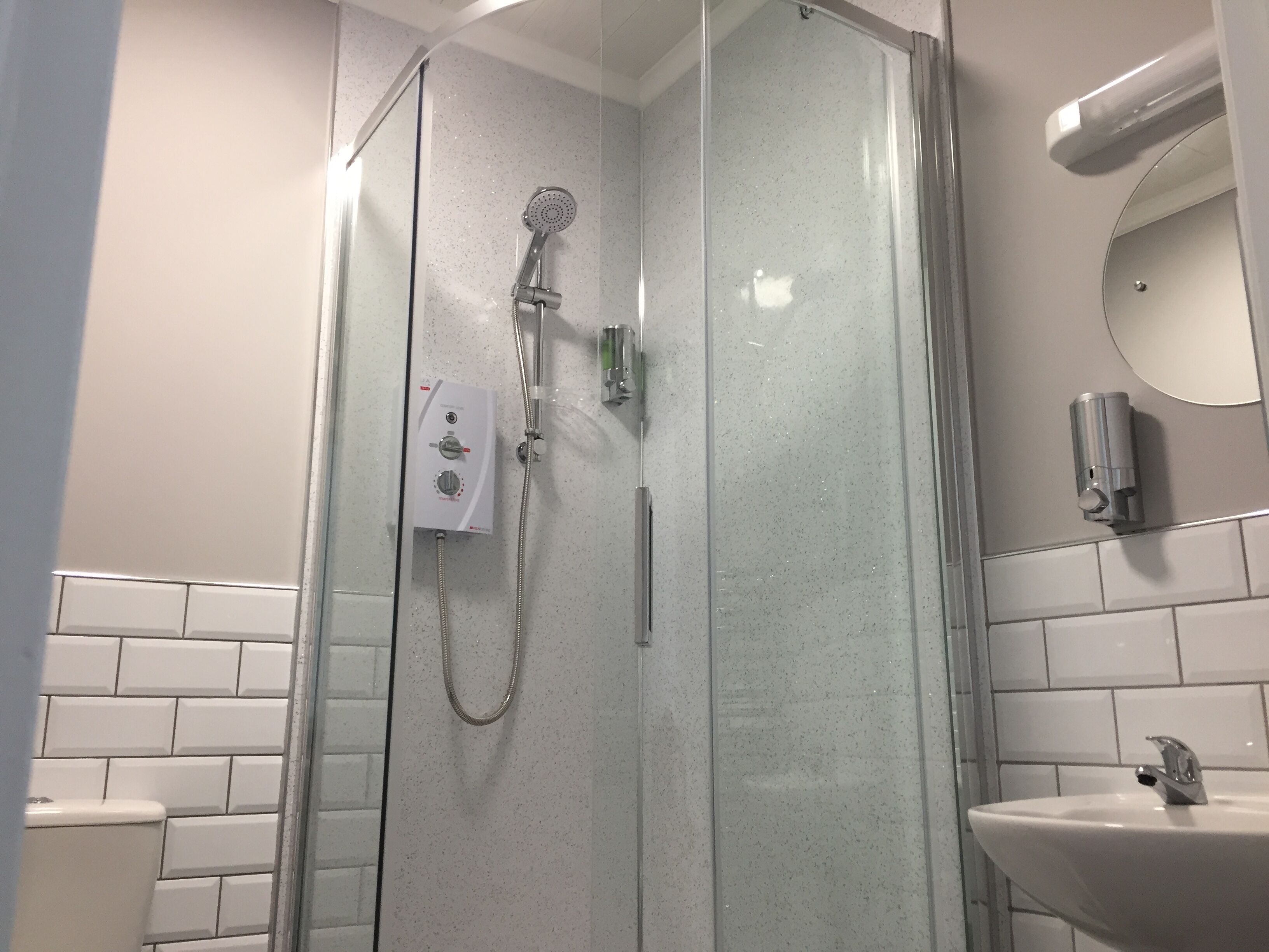 A glass-enclosed shower with a handheld showerhead and a wall-mounted control panel.