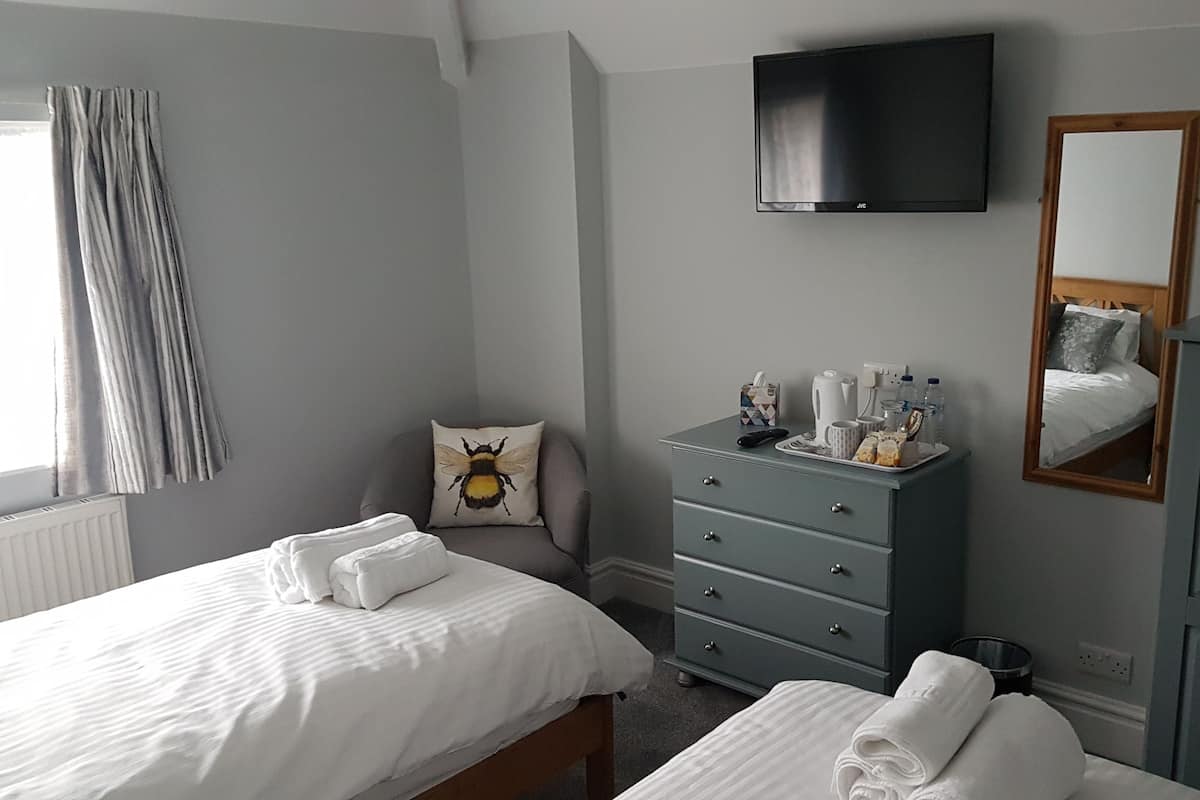Quarto de hotel com duas camas, uma cômoda, televisão, espelho e janela com cortinas.