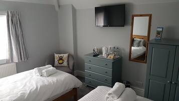 A hotel room with two beds, a dresser, a television, a mirror, and a window with curtains.