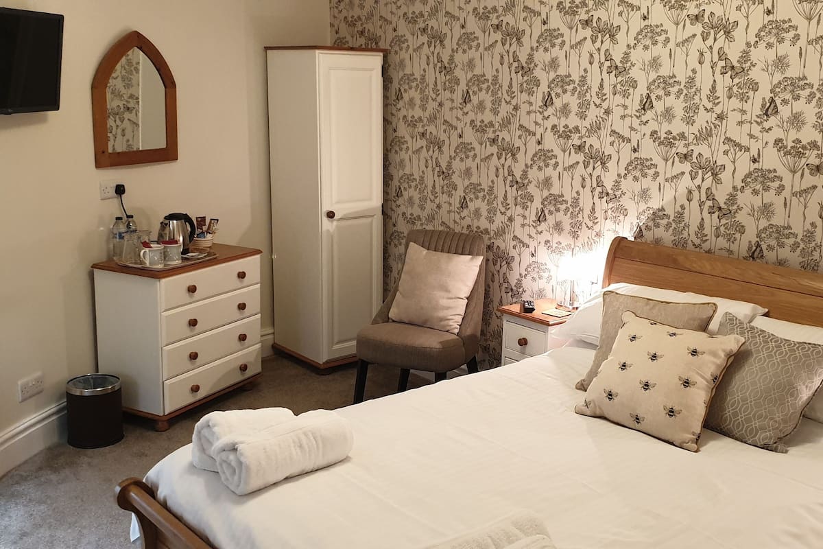 Quarto com cama, penteadeira, cadeira, mesa de cabeceira, espelho e guarda-roupa.