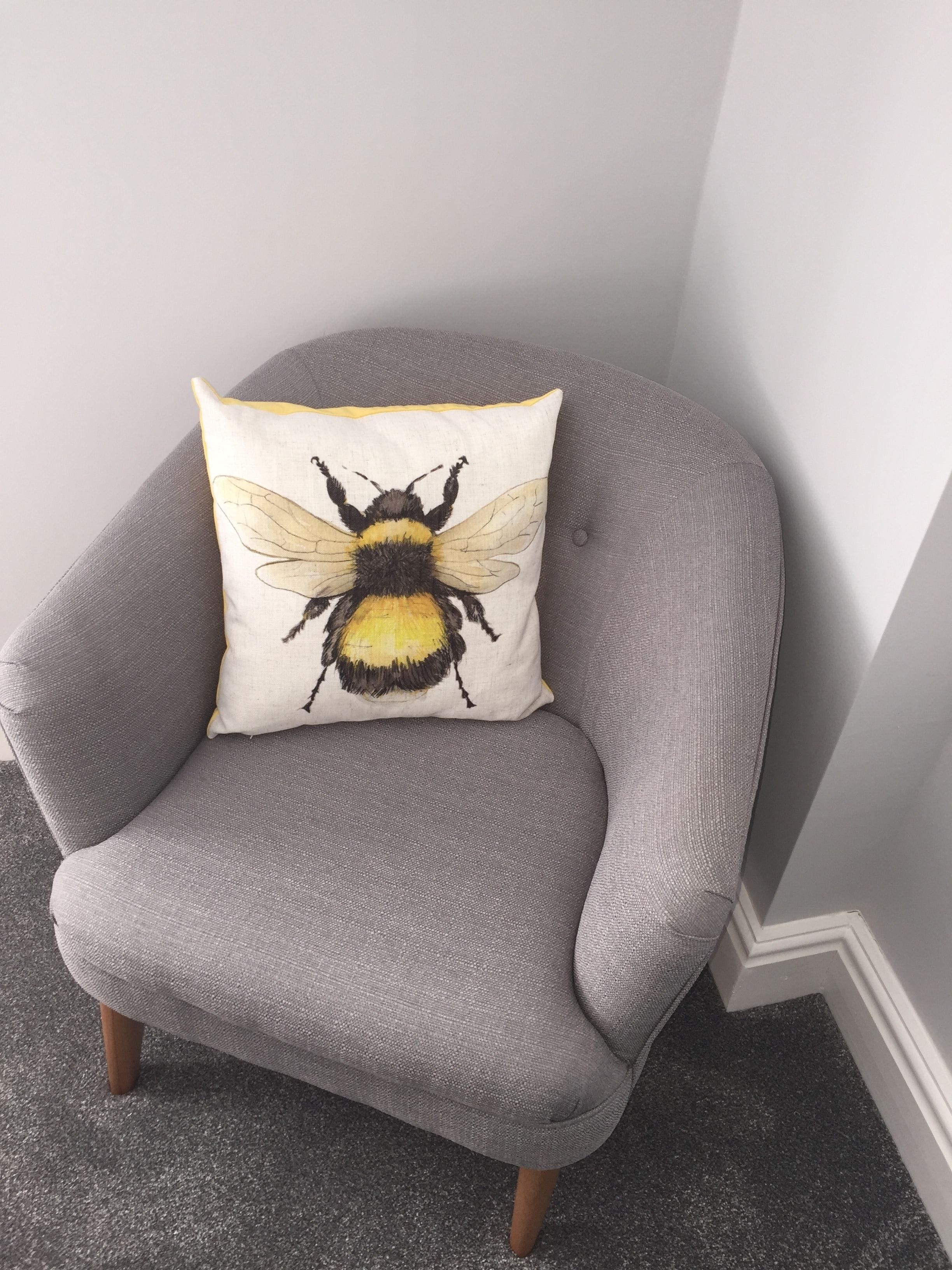 Un sillón gris con un cojín blanco con diseño de abeja.