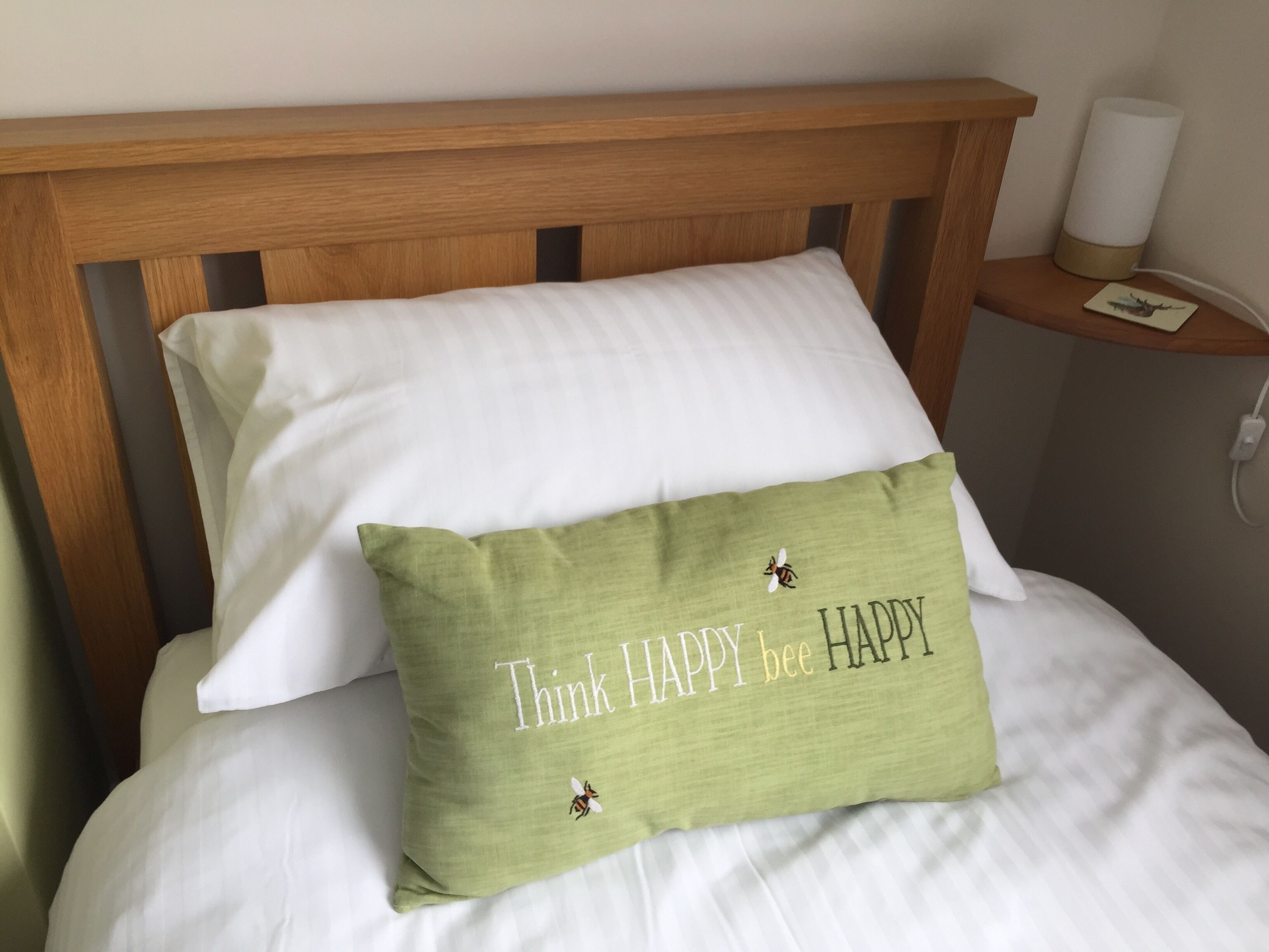 A bed with a wooden headboard, a white pillow, and a green pillow with the text "Think HAPPY bee HAPPY".