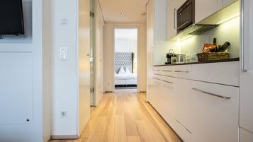 Una cocina moderna con armarios blancos, piso de madera y televisor de pantalla plana montado en la pared.