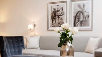 Una sala de estar con un sofá, una silla, un florero con rosas blancas y dos cuadros en la pared.