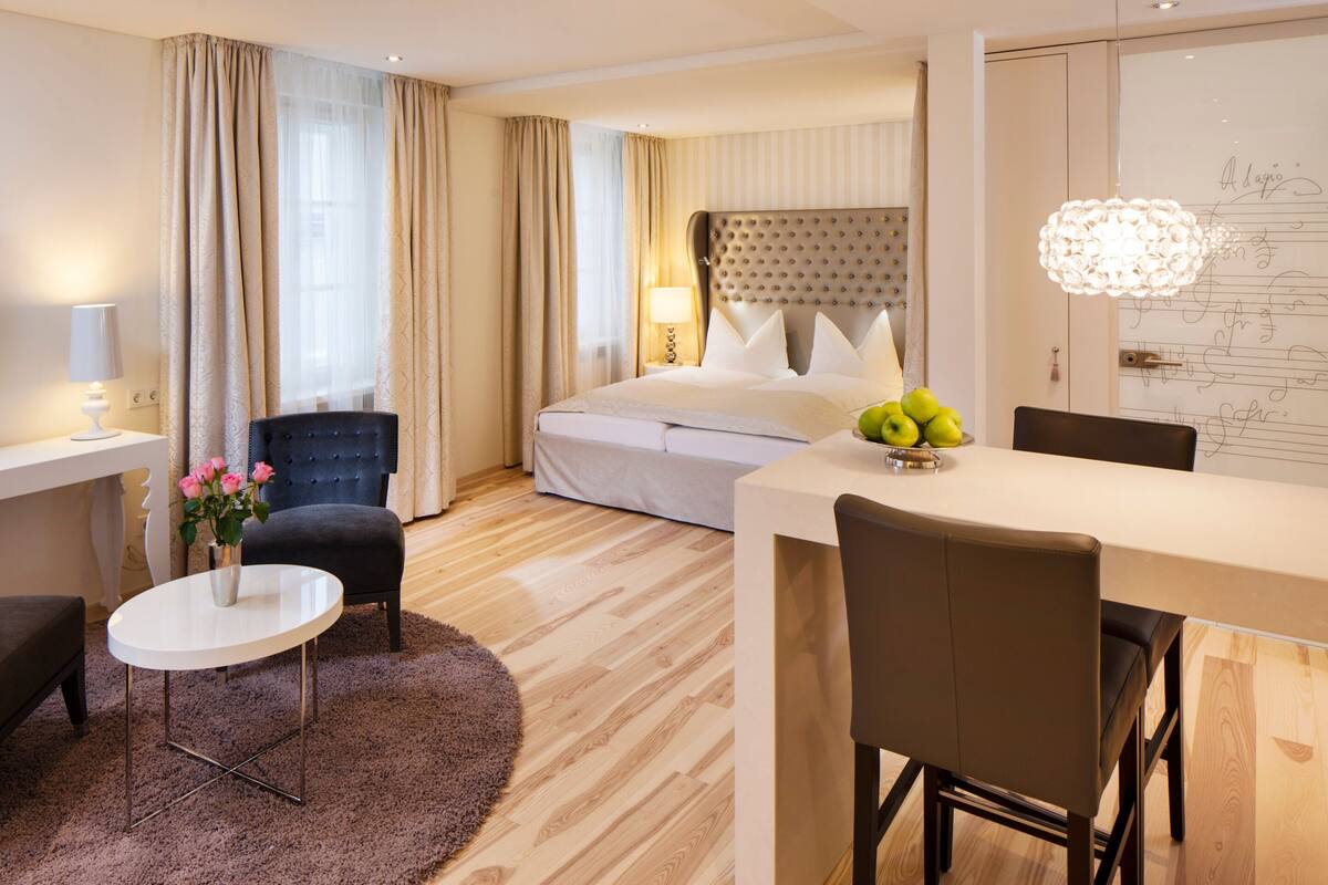 Une chambre d’hôtel comprenant un lit, un bureau, une chaise, une petite table et un vase décoratif avec des fleurs.