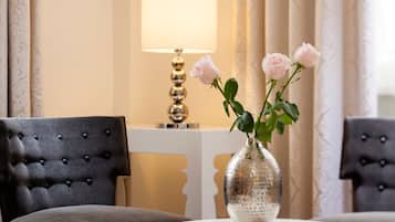 Una habitación con un sillón capitonado, una mesa redonda con un jarrón de rosas y una lámpara.