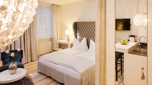 A hotel room with a large bed, a desk with a TV, and a small sitting area with a chair and a vase of flowers. - Hapimag Resort Salzburg (Salzburg)