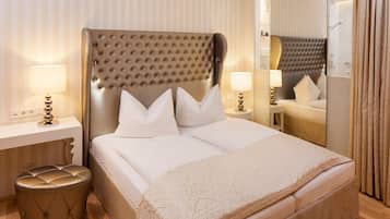 A neatly made bed with a tufted headboard, two bedside tables with lamps, a round ottoman, and a mirror reflecting the room.