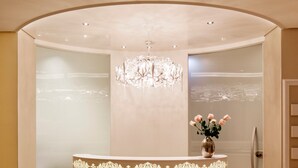 A reception area with a round counter, a chandelier, and a vase with flowers. - Hapimag Resort Salzburg (Salzburg)