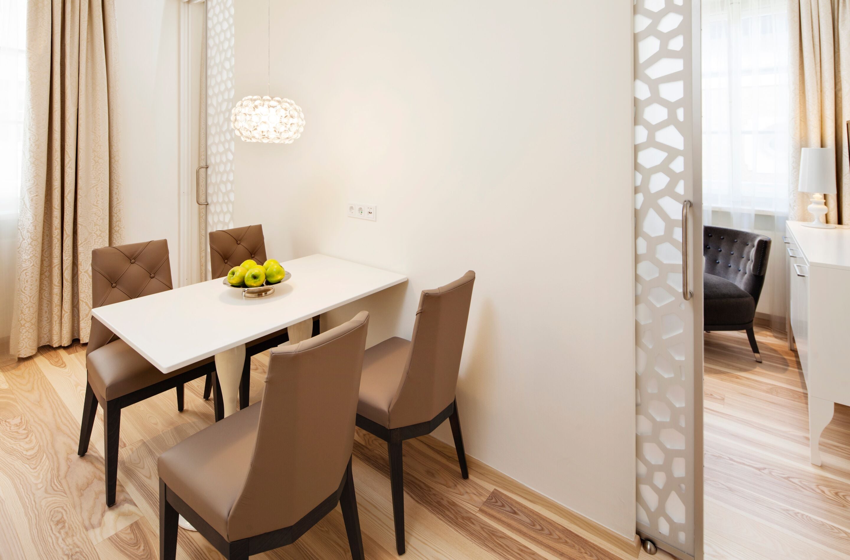 Een eethoek met een witte tafel, vier bruine stoelen en een schaal fruit.