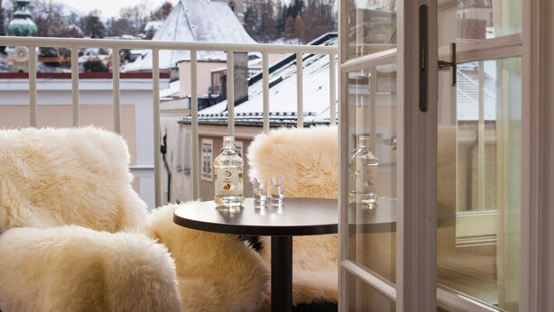 A balcony with a table and chairs, a bottle of liquor, and a view of a church spire. - Hapimag Resort Salzburg (Salzburg)