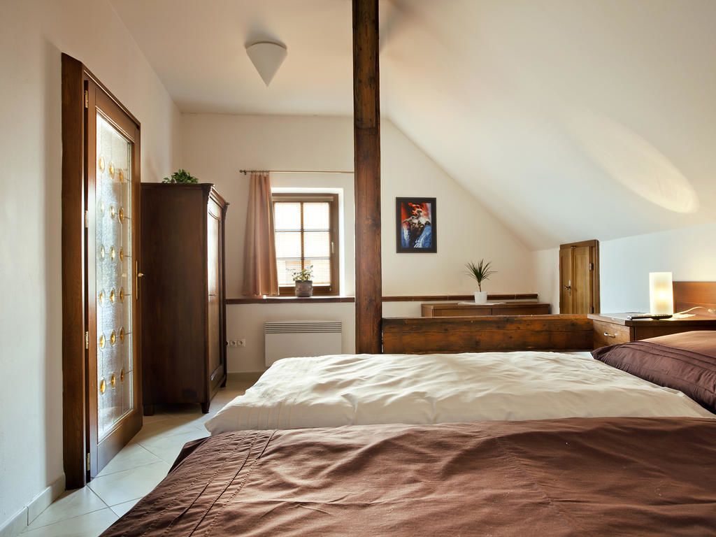 Un dormitorio con una cama grande, un armario de madera, una ventana con cortinas, una mesita de noche con lámpara y un cuadro en la pared.