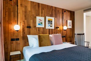Una cama bien hecha con una manta azul con textura, un cabecero de madera y tres cuadros en la pared.