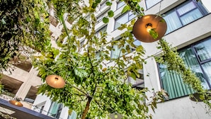 Un edificio con diseño arquitectónico moderno, que cuenta con ventanas amplias y un área de balcón con plantas colgantes e iluminación colgante.
