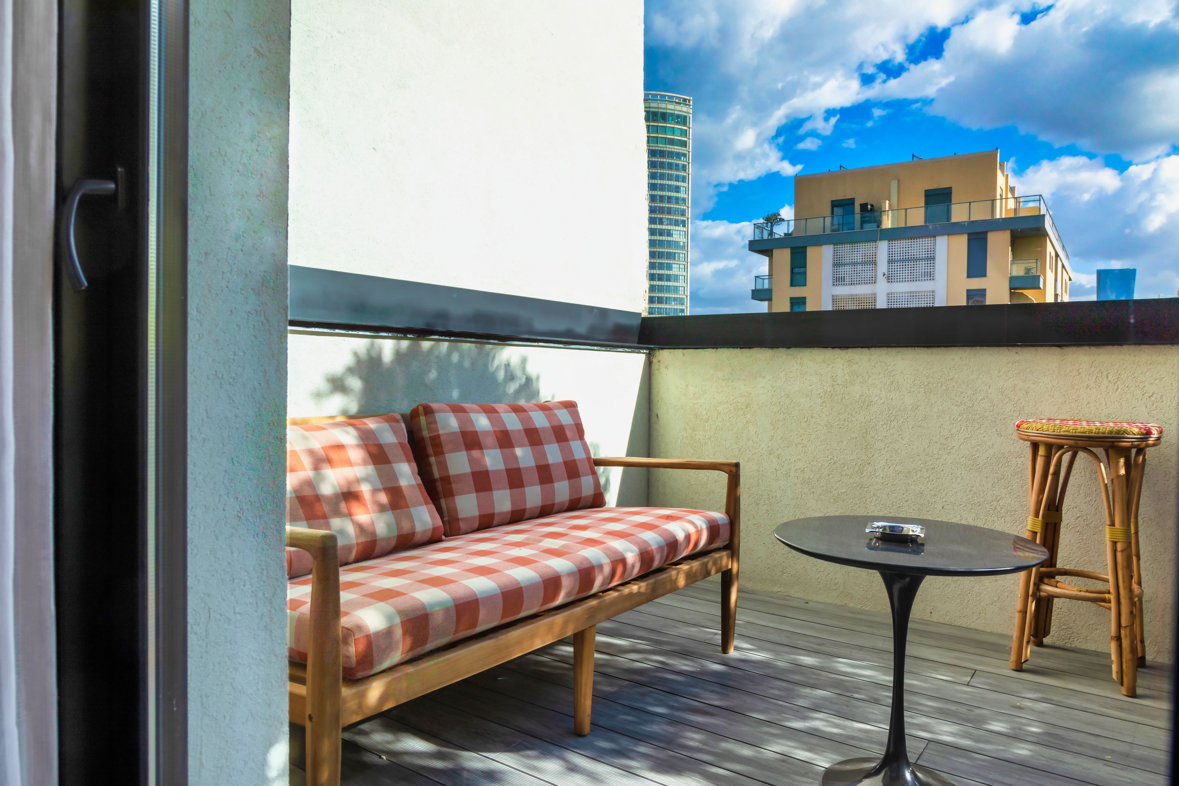 A balcony with a checkered sofa, a small round table, and a wicker chair.
