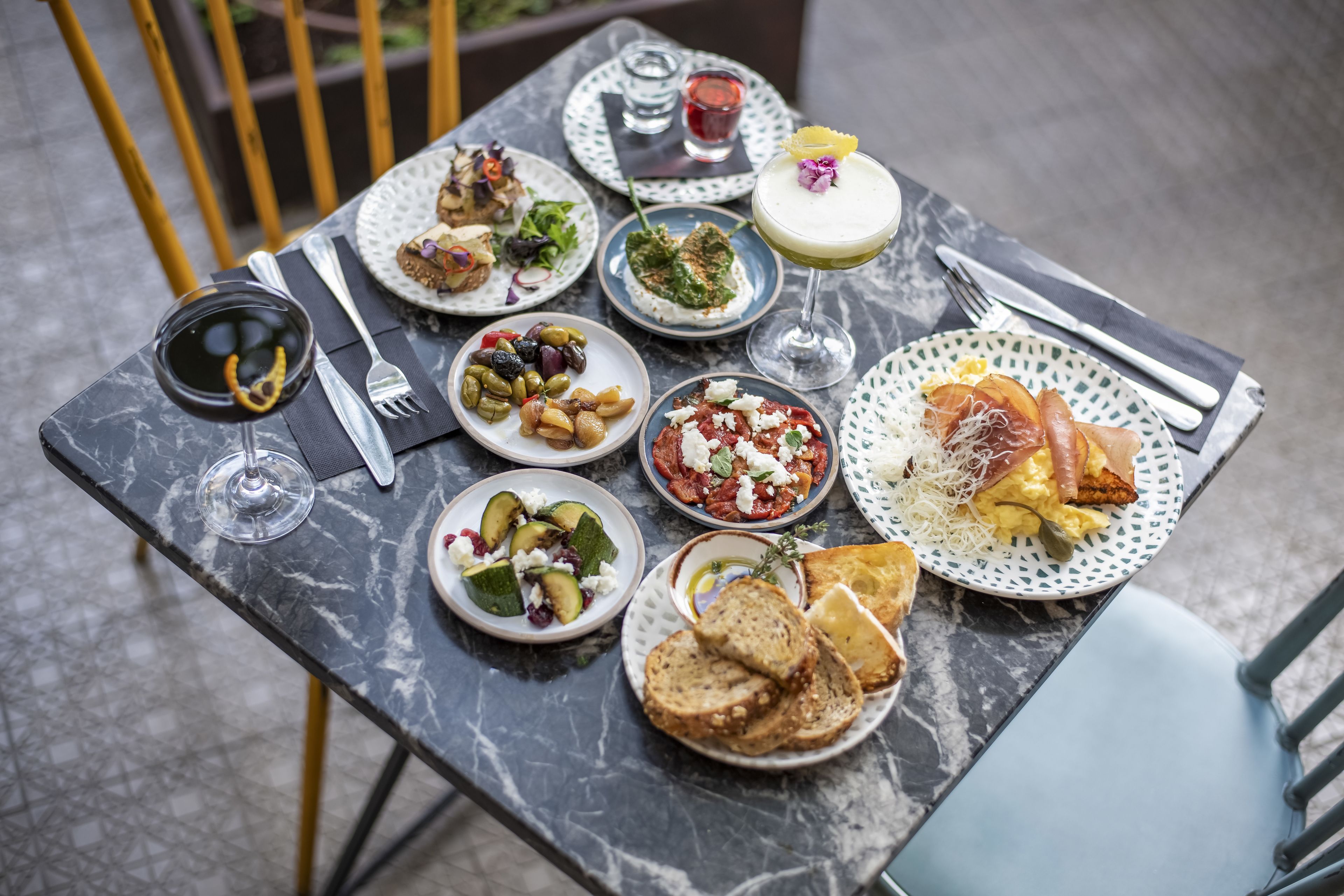 Ein mit verschiedenen Speisen, darunter Salate, Brot und Getränke, gedeckter Marmor-Esstisch, der eine Mahlzeit andeutet.