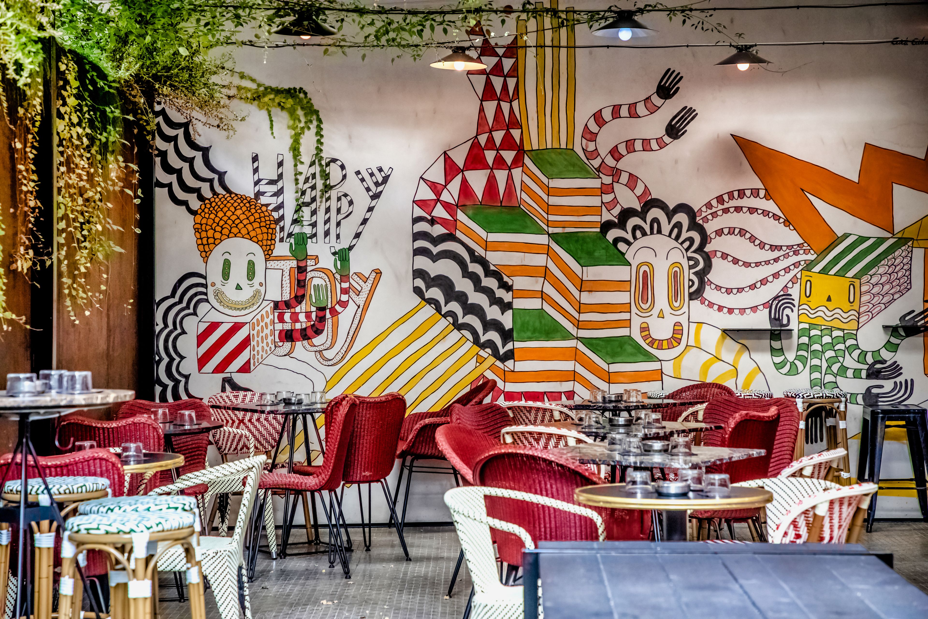Ein Restaurant mit farbenfrohen Wandgemälden, roten und weißen Korbstühlen sowie gedeckten Tischen.