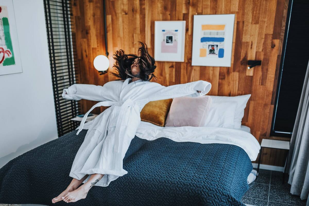 Una persona acostada en una cama en una habitación con paredes de madera, una colcha de color negro con textura y una bata de baño blanca.