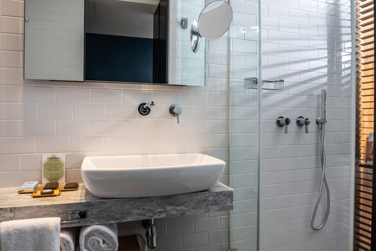 Un baño con lavamanos blanco, espejo, ducha y toallero.