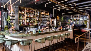 Una zona de bar con un mostrador curvo, varios taburetes altos y una variedad de botellas y vasos en estantes.