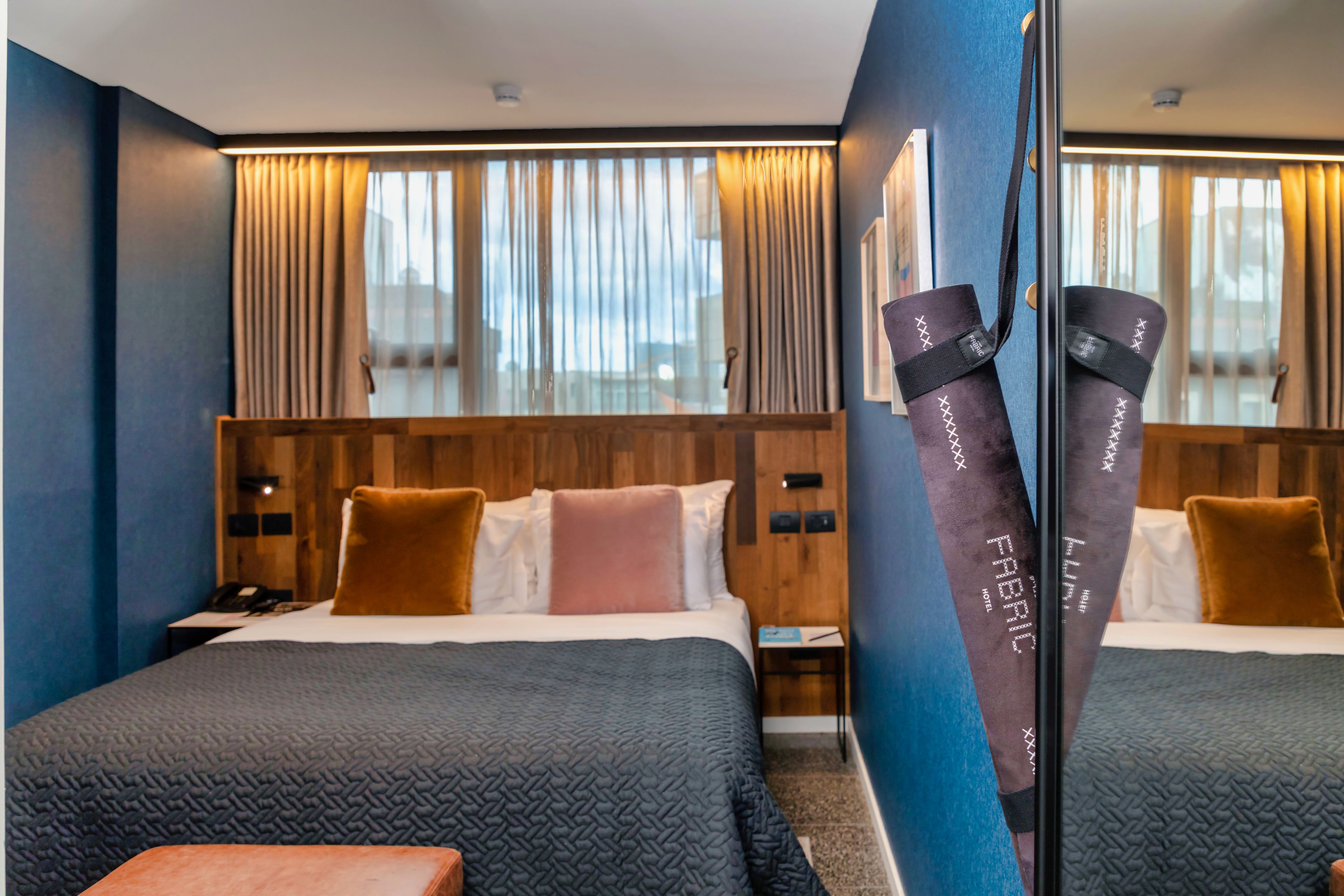 Une chambre d’hôtel avec deux lits, une tête de lit en bois, un grand miroir et une vue sur la ville par la fenêtre.