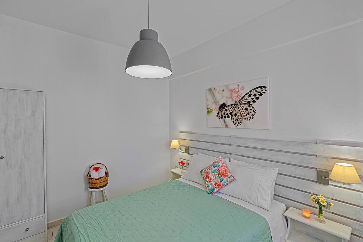 A bedroom with a bed, a nightstand, a wall-mounted lamp, a decorative wall piece, and a wardrobe.