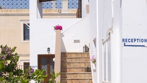 A white building with a reception area, a staircase, and a balcony. - Letta's Apartments (Syros)