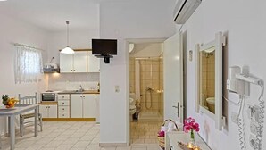 A modern hotel room with a bed, a small desk, a mirror, and a bathroom with a shower and toilet. - Letta's Apartments (Syros)