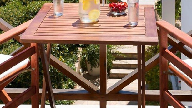 A wooden table with a pitcher of lemonade, a glass of water, and a bowl of cherries on a balcony. - Letta's Apartments (Syros)