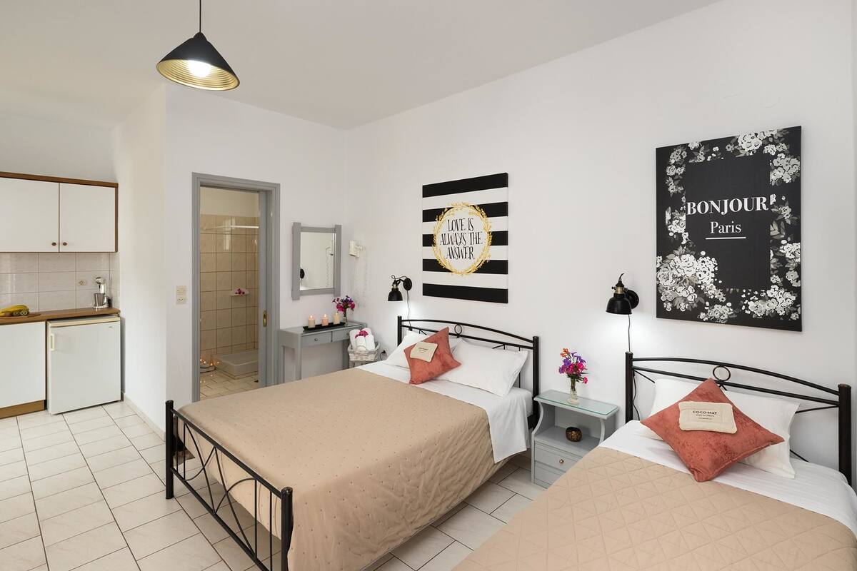 A bedroom with a bed, bedside tables, a nightstand, a mirror, and a wall with a 'Bonjour Paris' sign.