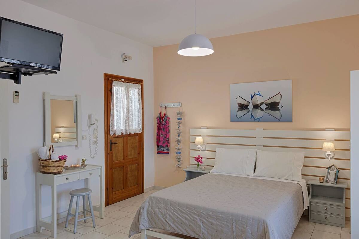 A bedroom with a bed, bedside tables, a TV, a desk with a chair, a mirror, and a door.